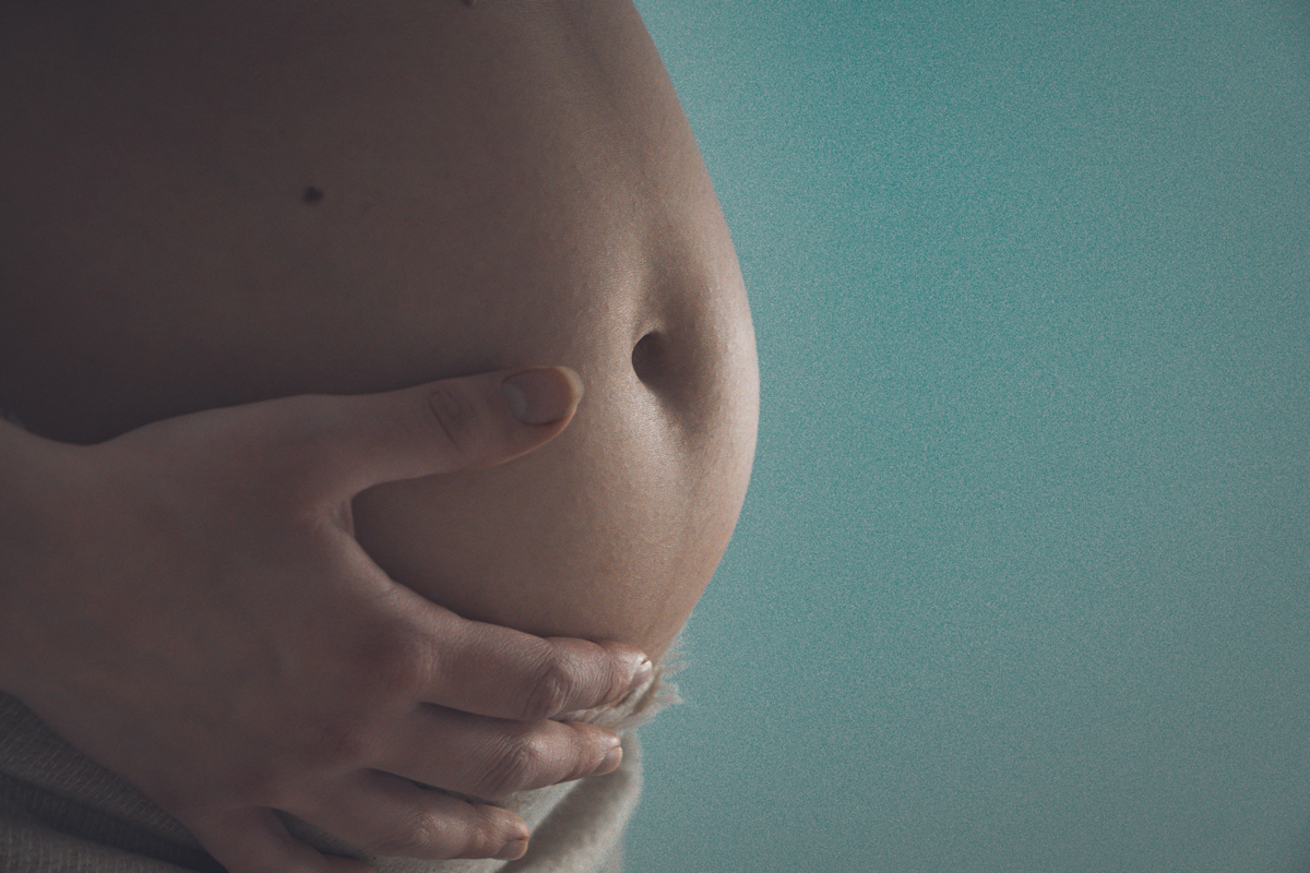 Gros plan sur le ventre du femme enceinte dont ça main droite touche le bas du ventre