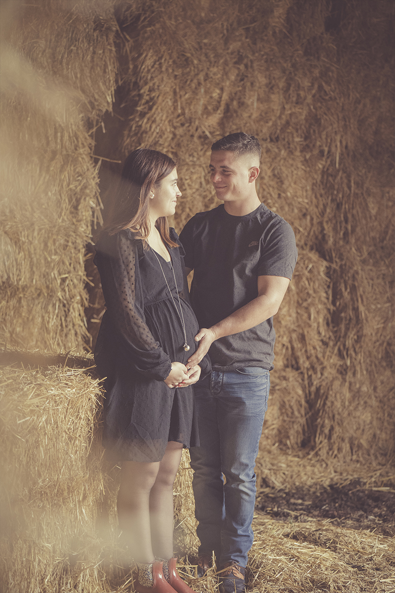 Couple dans une grange de paille pour une séance photo de grossesse