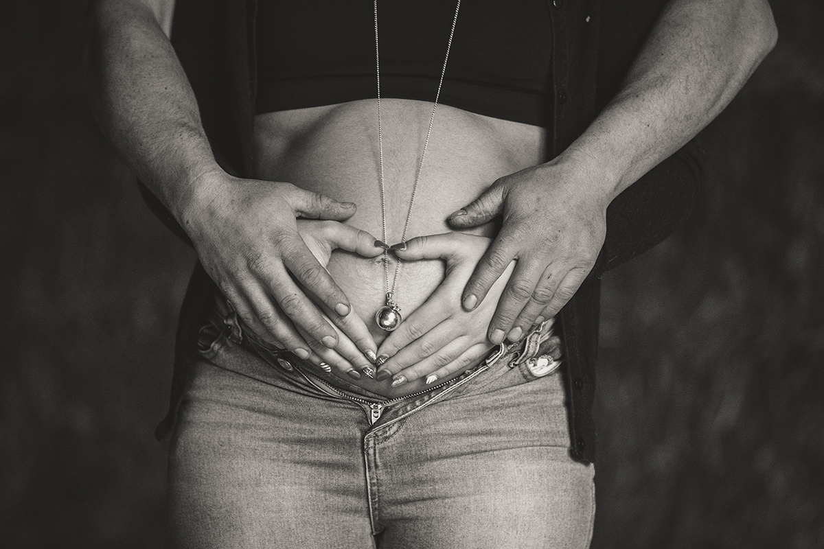 Quatre mains formant un cœur sur le ventre rond d'une femme enceinte