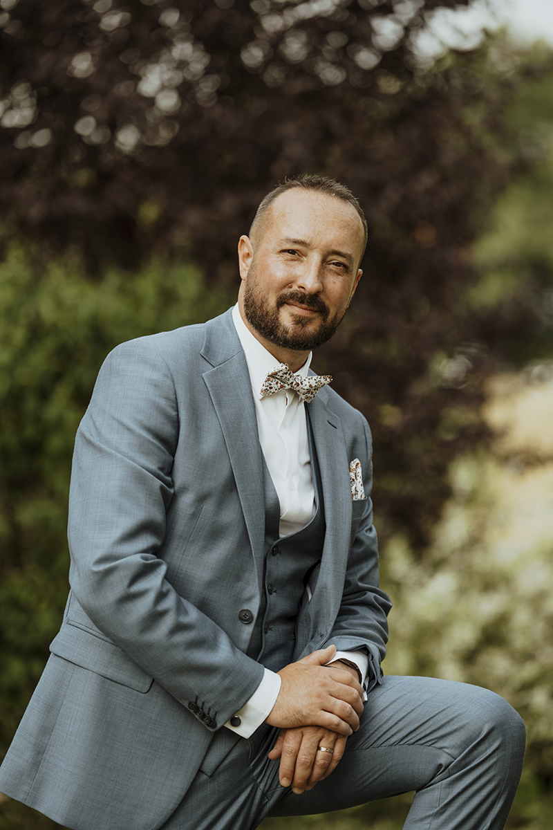 Marié posant dans un costume bleu clair avec un nœud papillon, devant un fond naturel verdoyant lors d'un mariage à Limoges